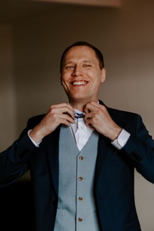 Groom adjusts his bowtie while getting ready in formal attire.