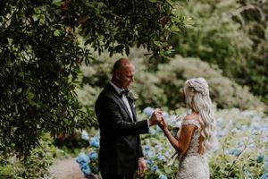 Couple shares intimate moment in garden surrounded by blooming hydrangeas.