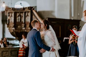 Couple sharing their first kiss during wedding ceremony in historic church interior.