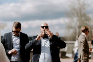 Wedding guest in sunglasses and suit enjoys drinks during outdoor reception.