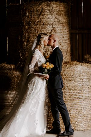Romantic wedding portrait with couple embracing in front of rustic barn wall with sunlit glow.
