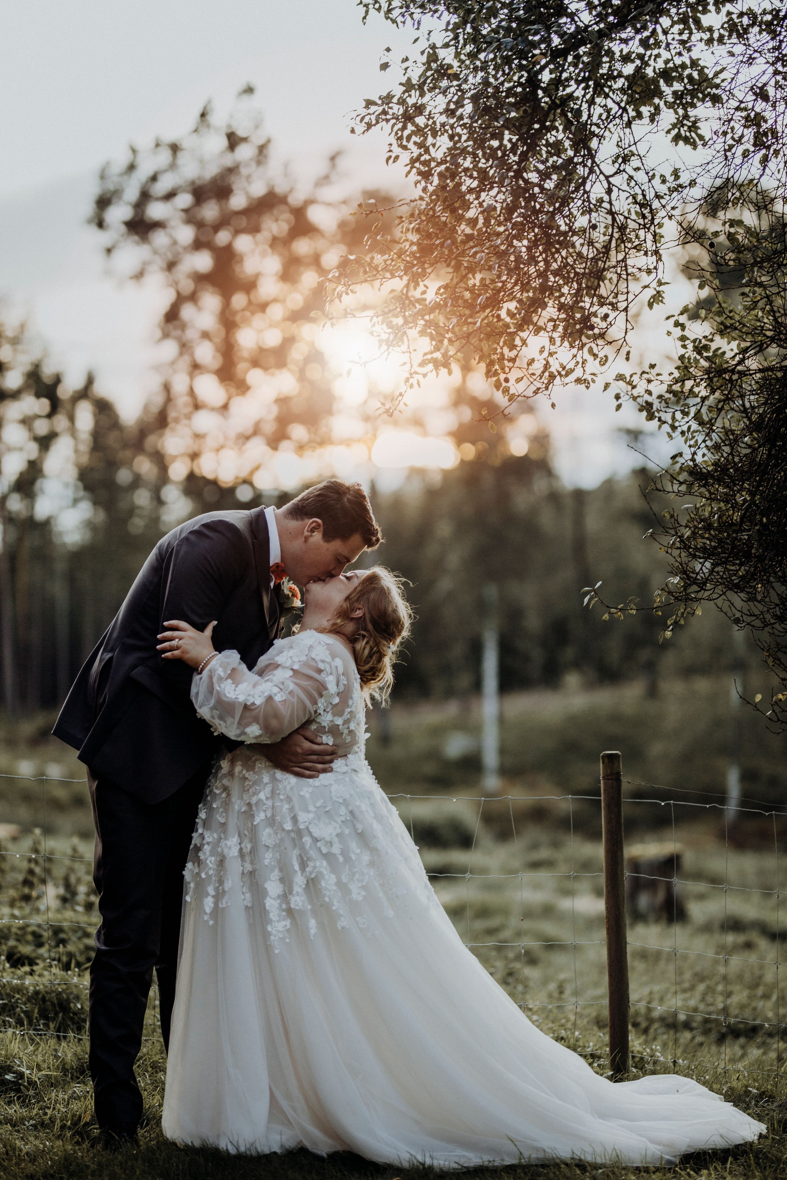 Wedding couple silhouetted against golden sunset in countryside setting.