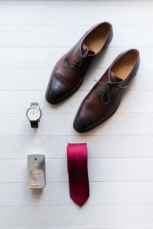 preparatifs du marie, la photo met en avant le detail de la tenue du marie (chaussures, montres, cravate, parfum)