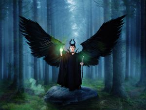 Child dressed as Disney character Maleficent with wings and glowing staff standing on a boulder in a menacing forest.