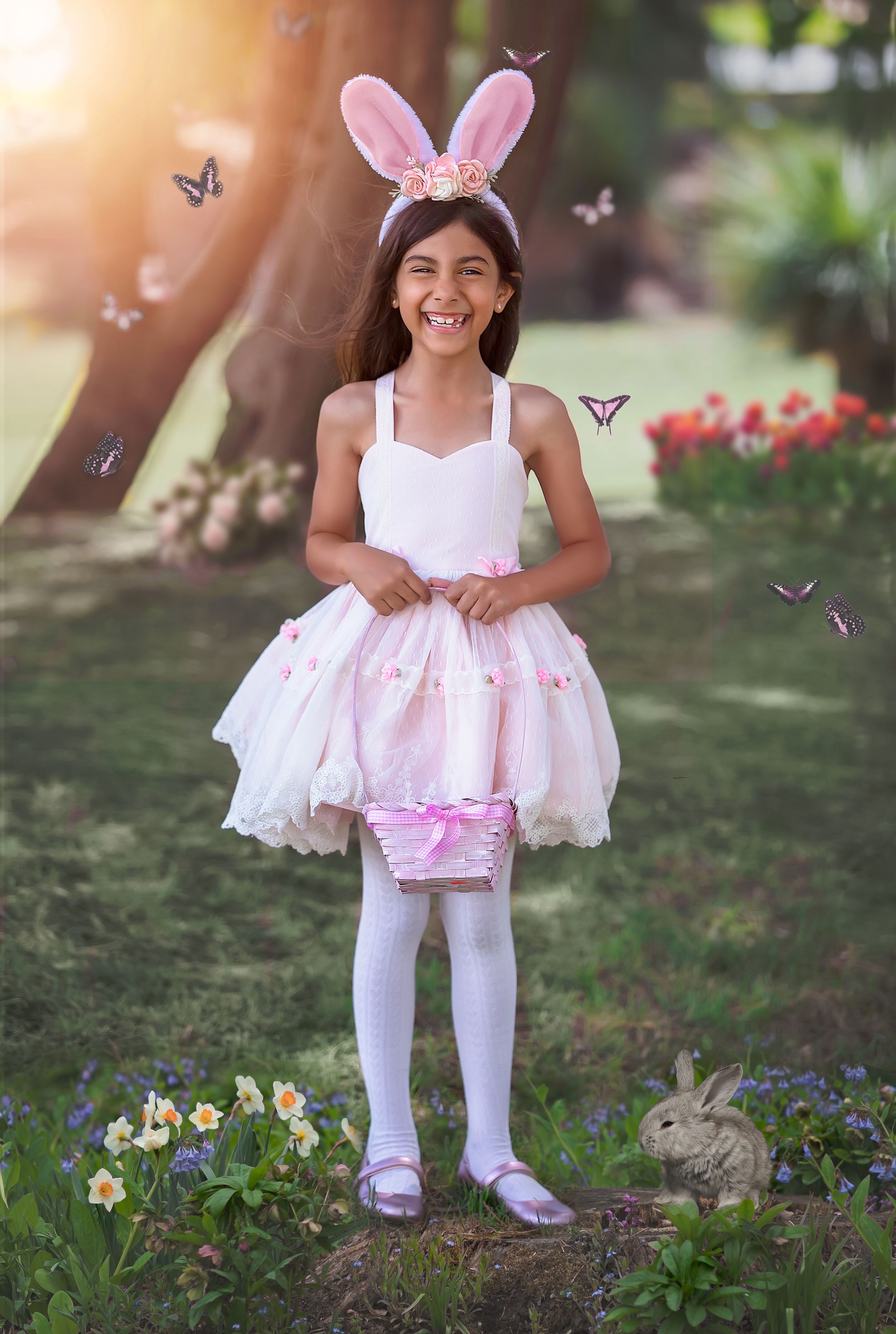 Little girl wearing Easter Bunny ears surrounded by butterflies, with a bunny at her feet, holding an Easter hunt basket