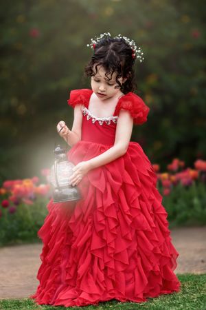 Little girl in red frilly dress holding a lantern while standing in front of a tulip garden.