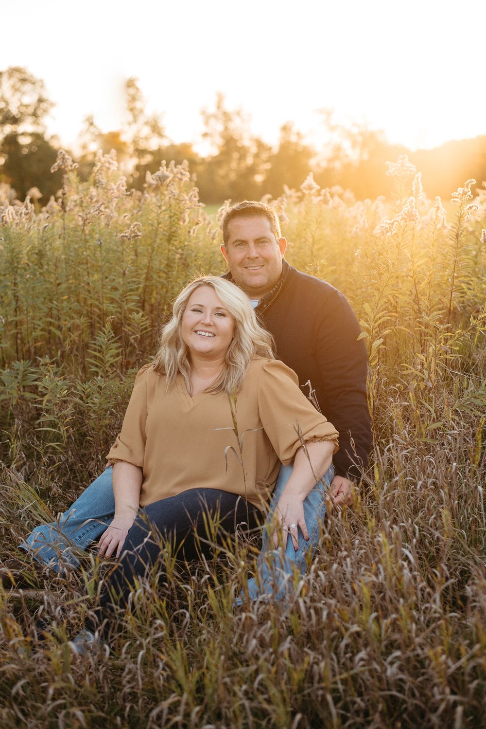 Couple posing together in tall grass field during golden hour sunset.