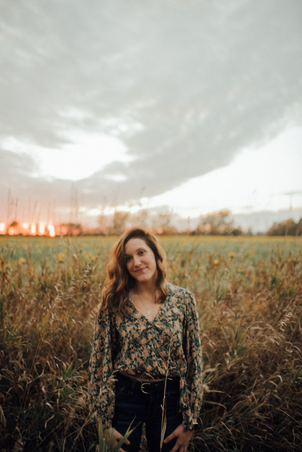 Person in floral top standing in field during golden sunset.