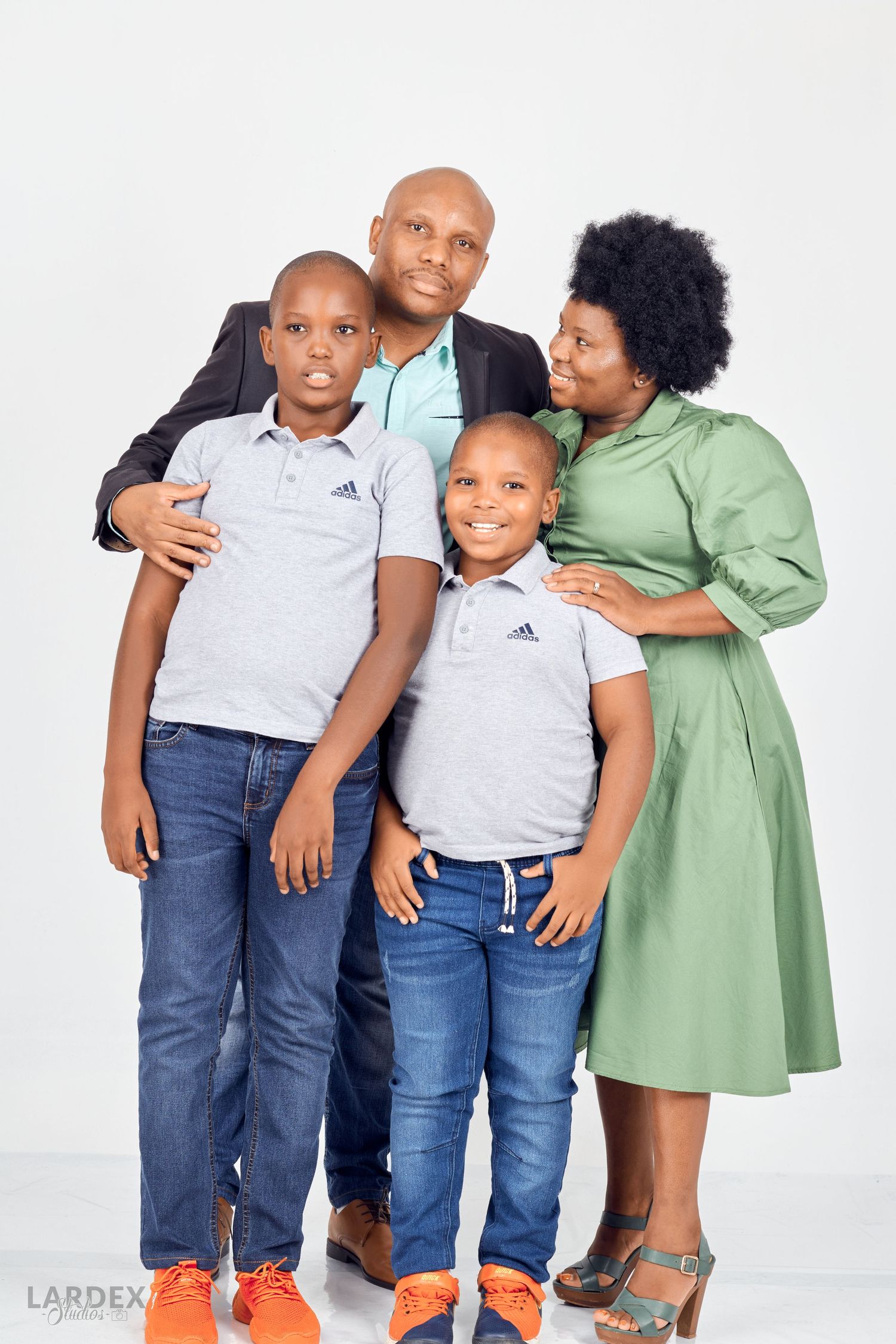 Happy family portrait of parents and two children wearing casual attire against white background.