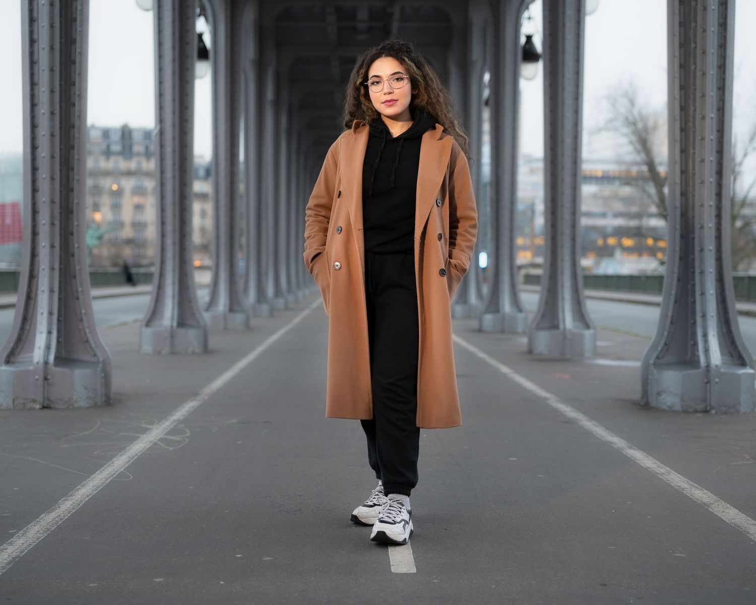 Urban fashion shoot under concrete bridge columns with camel coat.