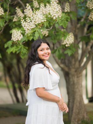 Beautiful high school senior portrait outdoors with white dress and flowering tree in background.