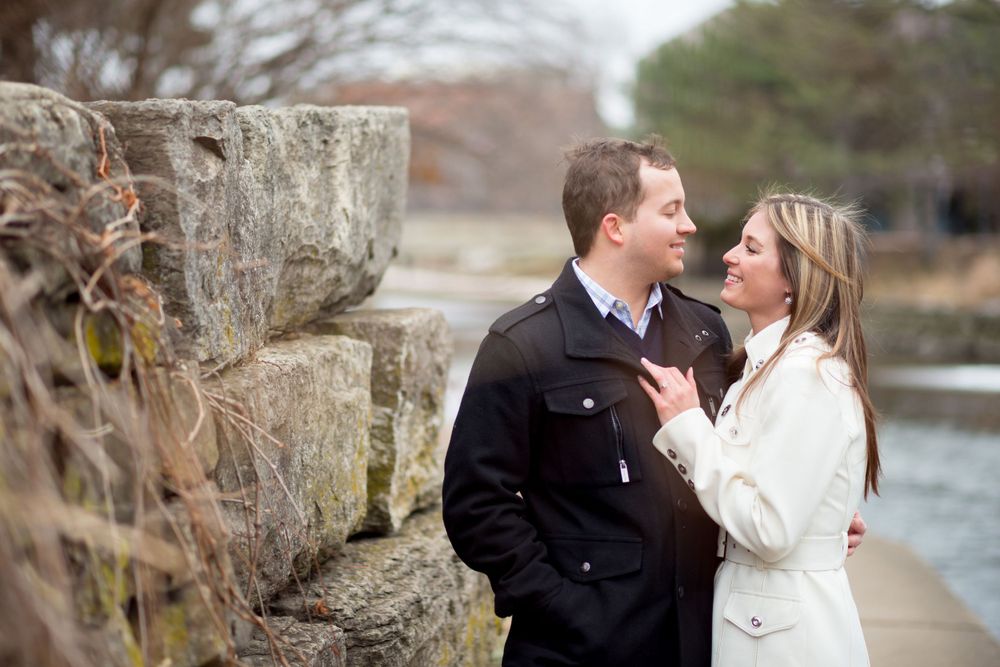 A recently engaged couple embracing while standing along the banks of the Naperville Riverwalk.