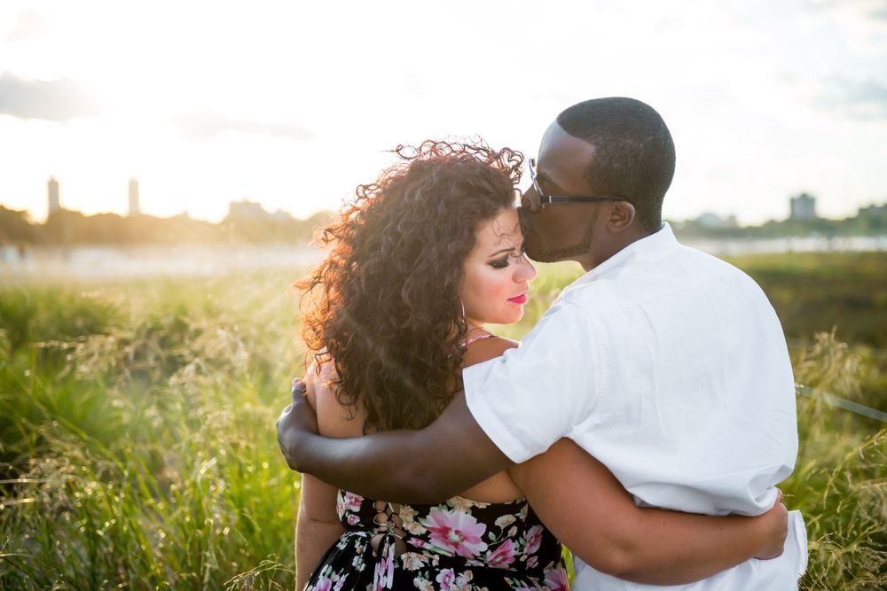 A recently engaged interacial couple embracing among wild grasses during sunset at Montrose Beach in Chicago, IL.