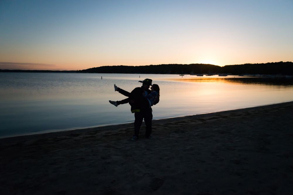Silhouette at dusk of a recently engaged couple walking along the beach in Lake Geneva, WI.