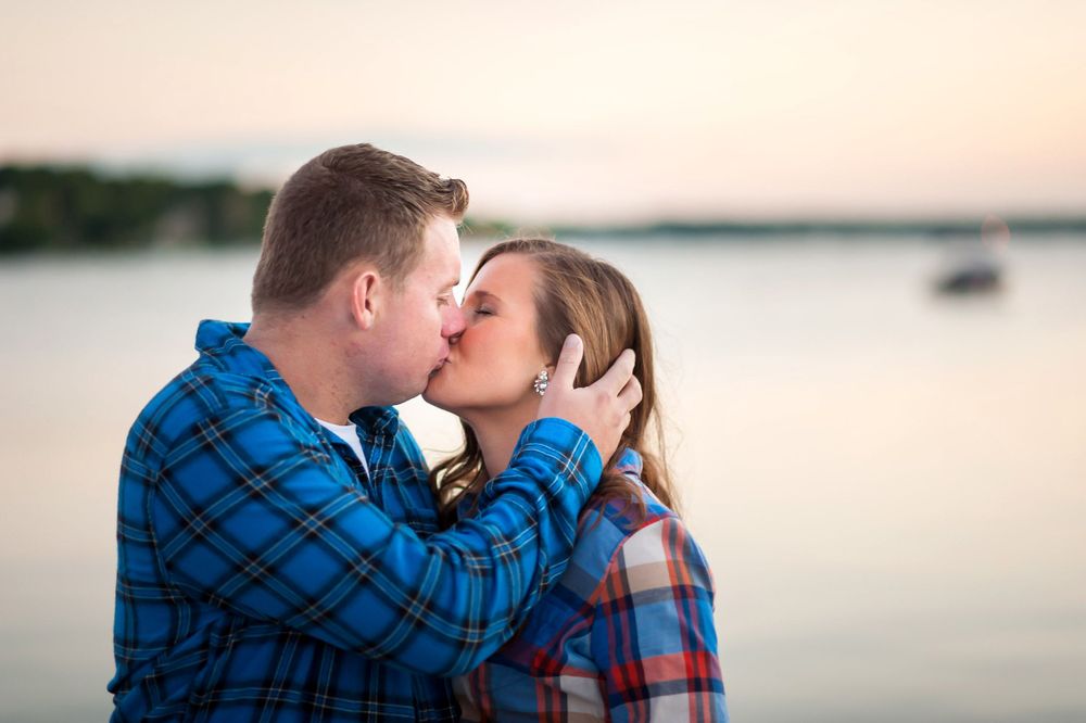 A recently engaged couple kissing on the beach at dusk with Lake Geneva in the background.
