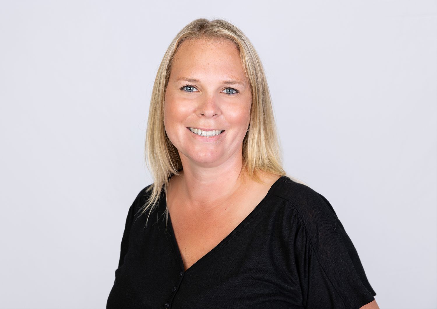 Professional headshot of a smiling blonde woman wearing a black top on a white background.