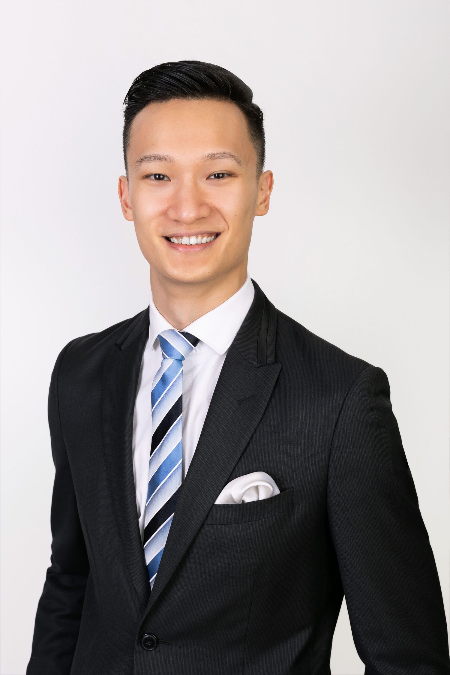 Professional headshot of a smiling young Asian man in a black suit and striped tie.
