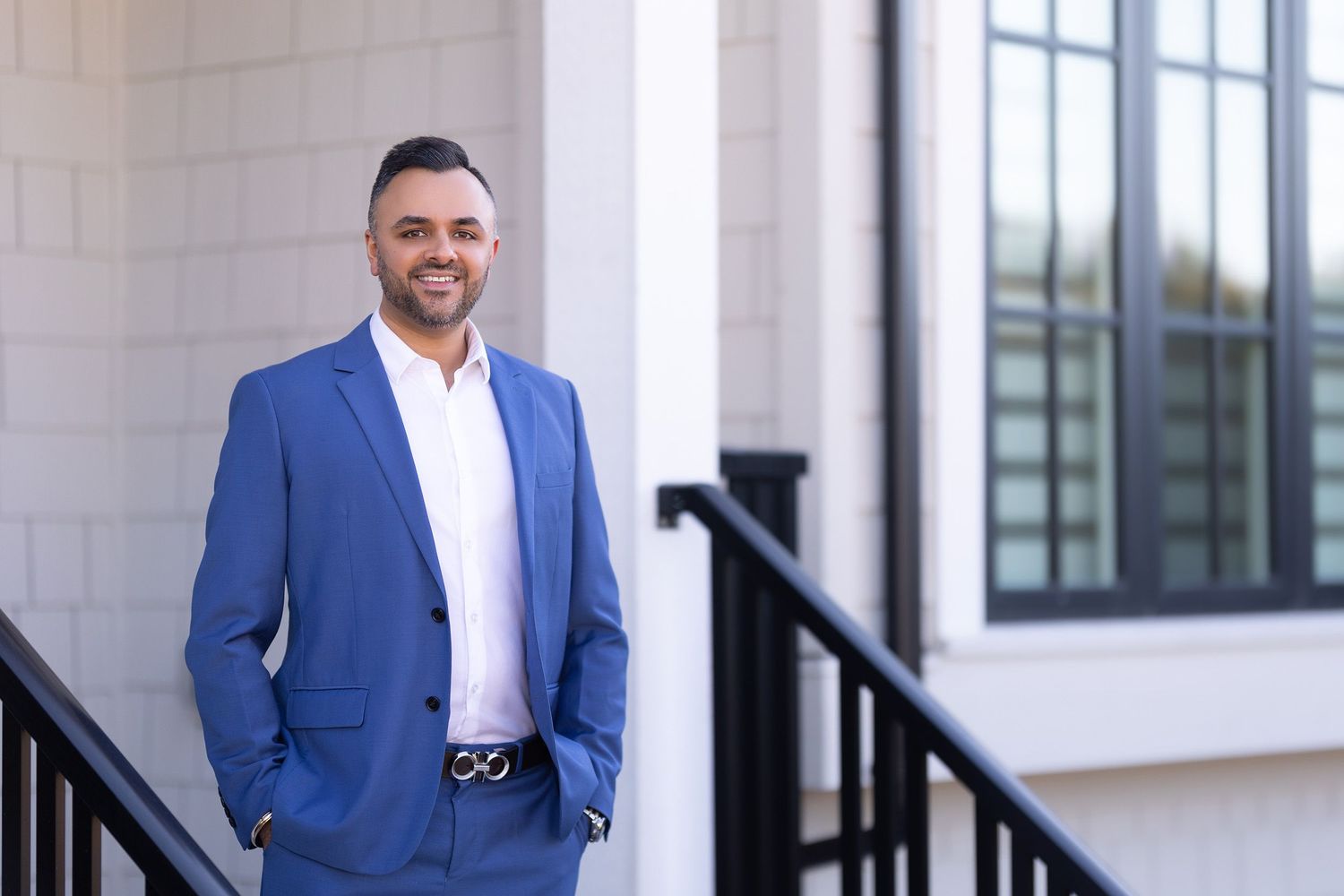 Professional man in blue blazer smiling on outdoor stairs near modern building.