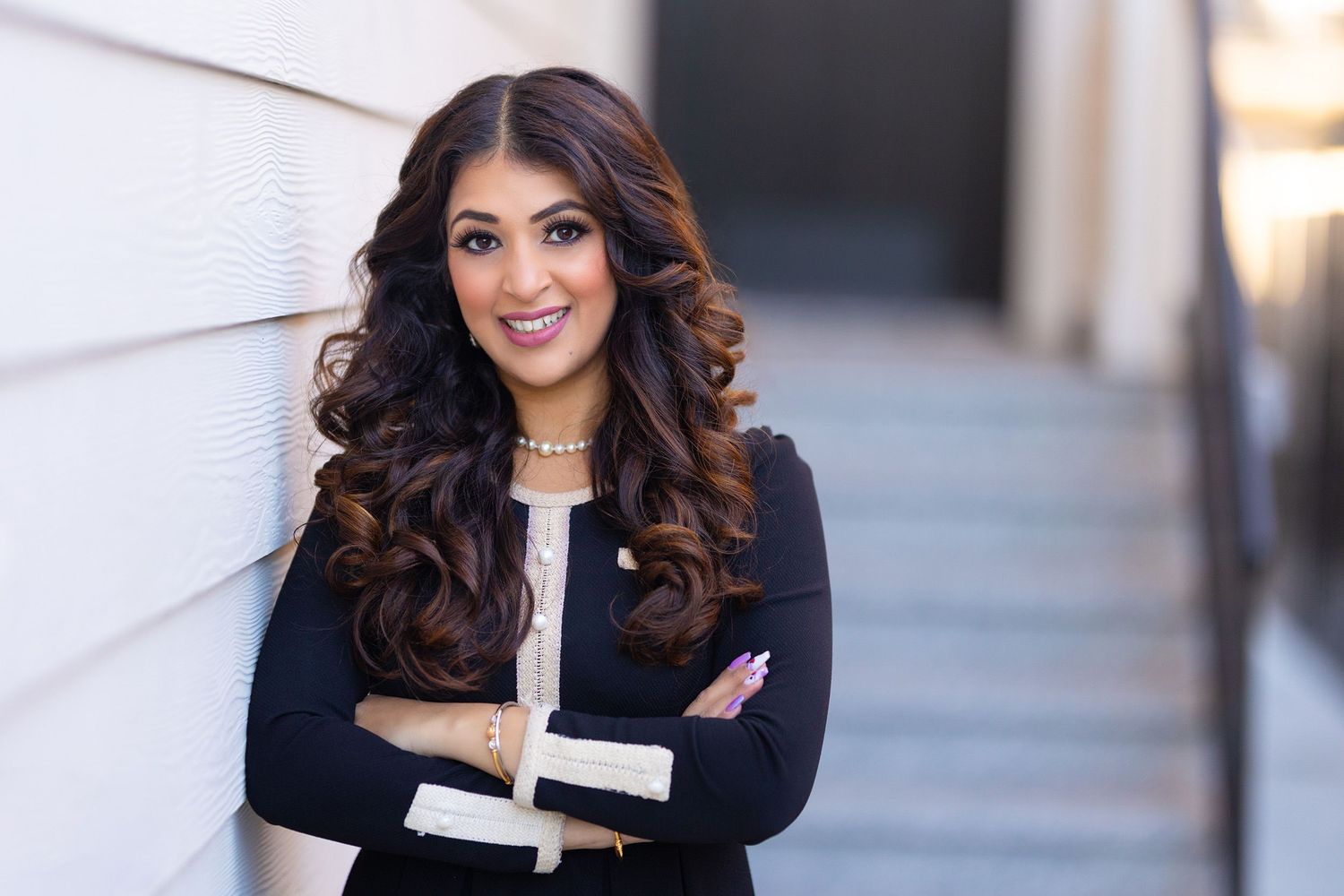 Professional woman in navy blazer with crossed arms smiling against white wall.