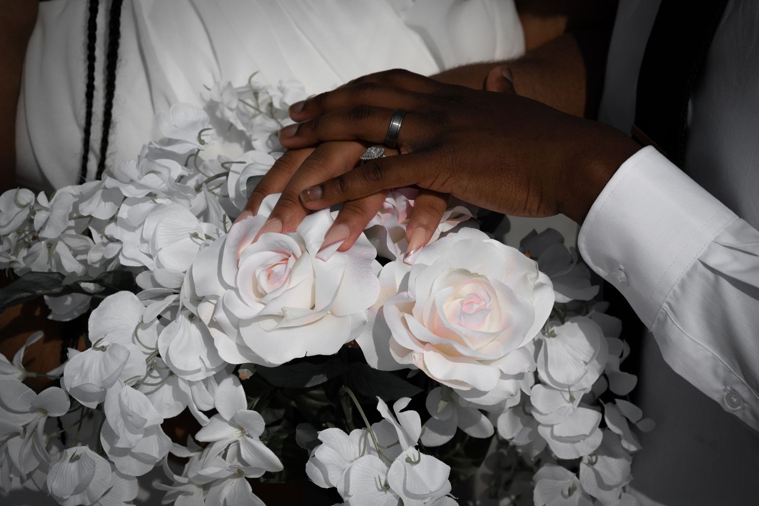 Close-up of hands holding white roses and flowers in black and white.