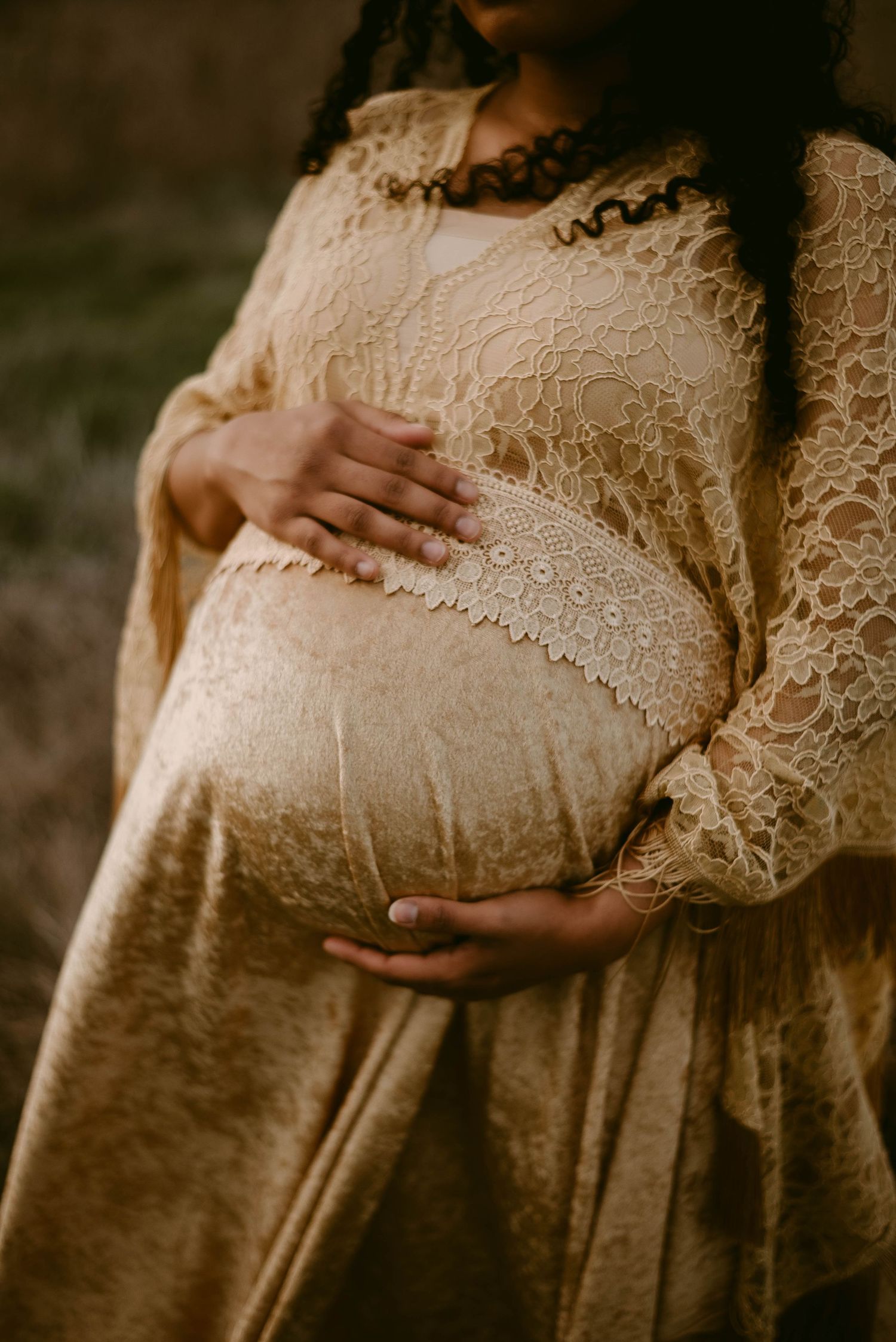 A detailed shot of intricate cream lace maternity dress with hands cradling the baby bump.