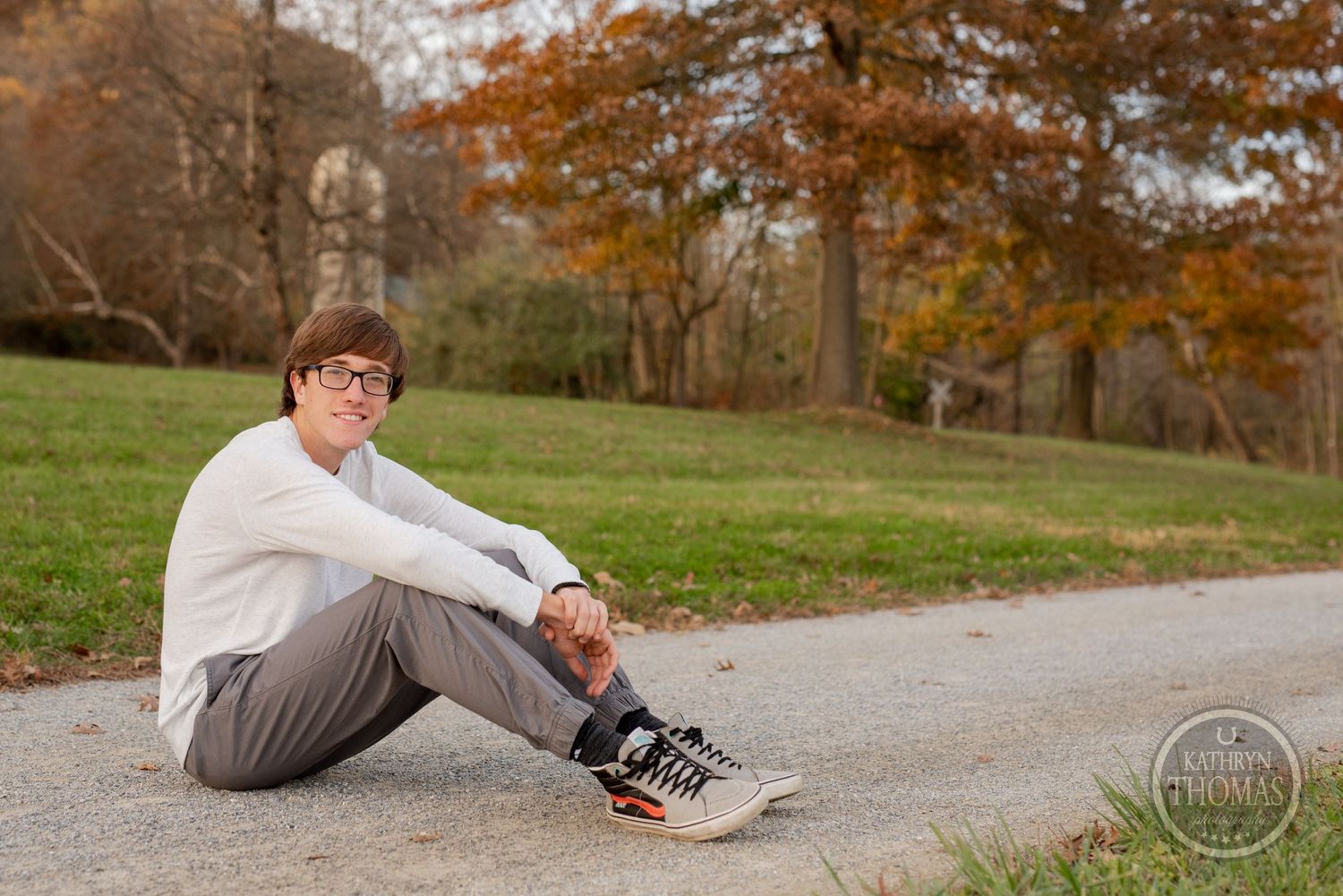 A person sits on a path with autumn trees and grass in the background.