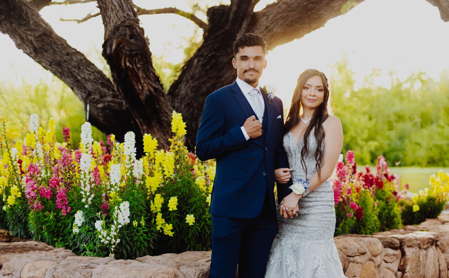 A wedding photo featuring a couple posing by a tree with colorful flowers in bloom.