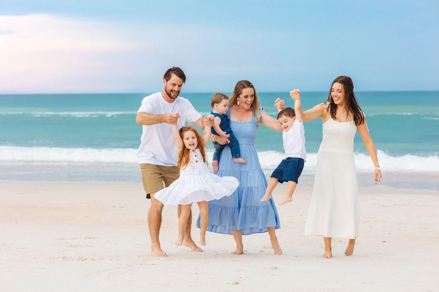 Happy family in white and blue outfits playing together on sandy beach.