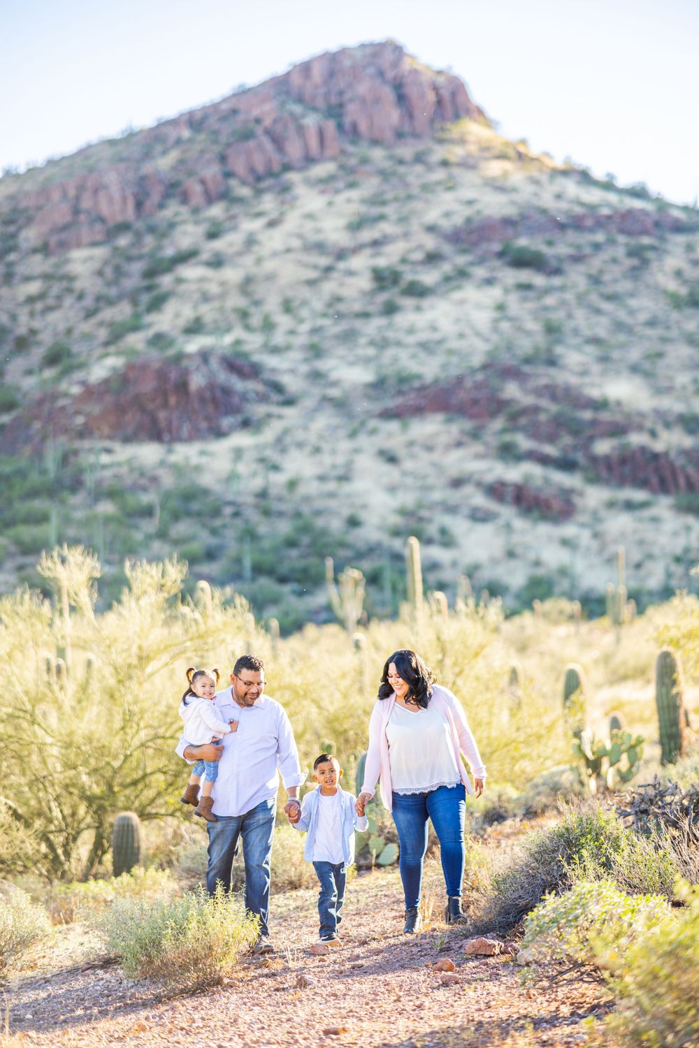Family walking together on a desert trail with red rock mountains and saguaro cacti in the background.