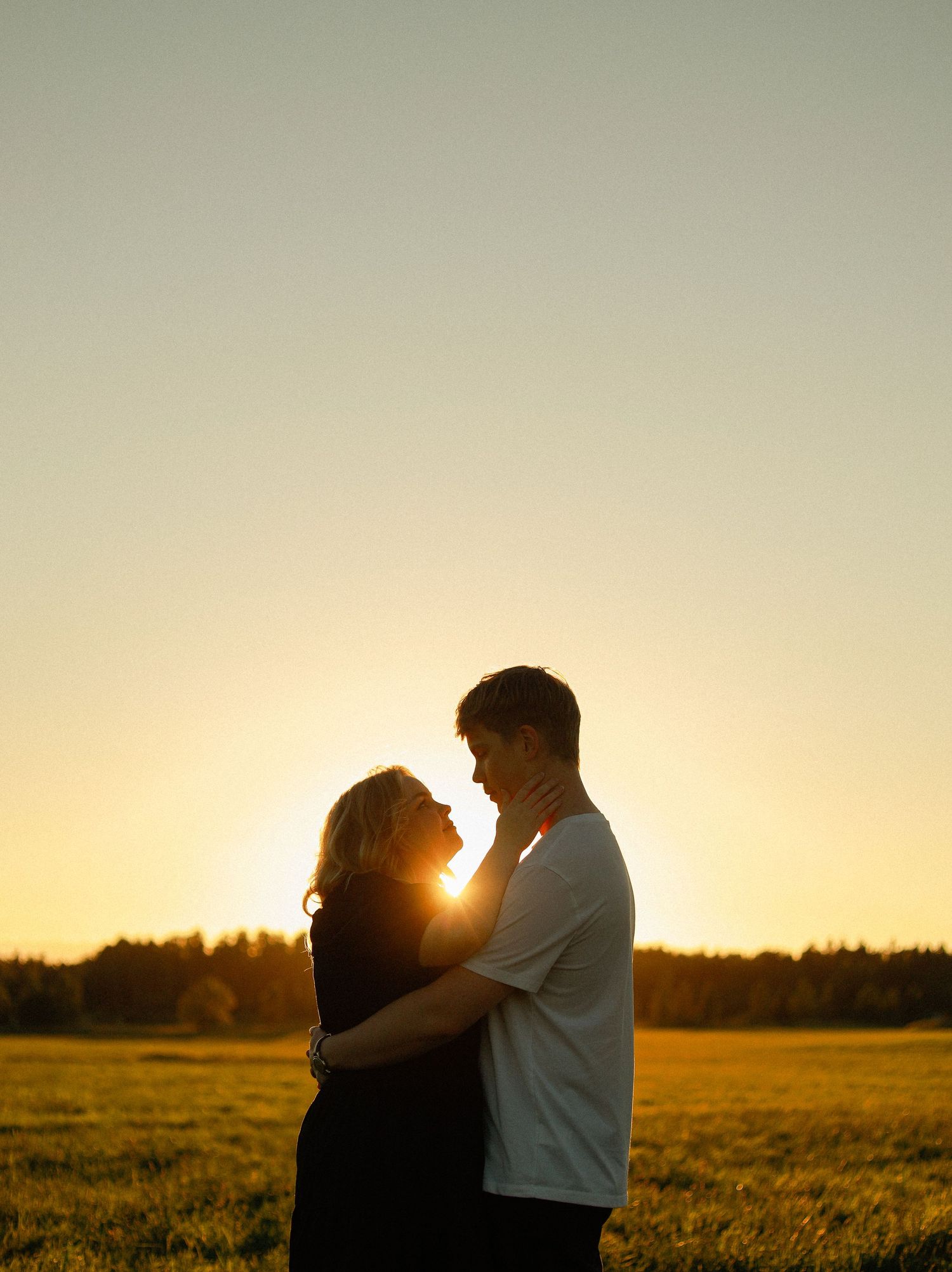 Silhouette of couple embracing in a field during golden hour sunset.