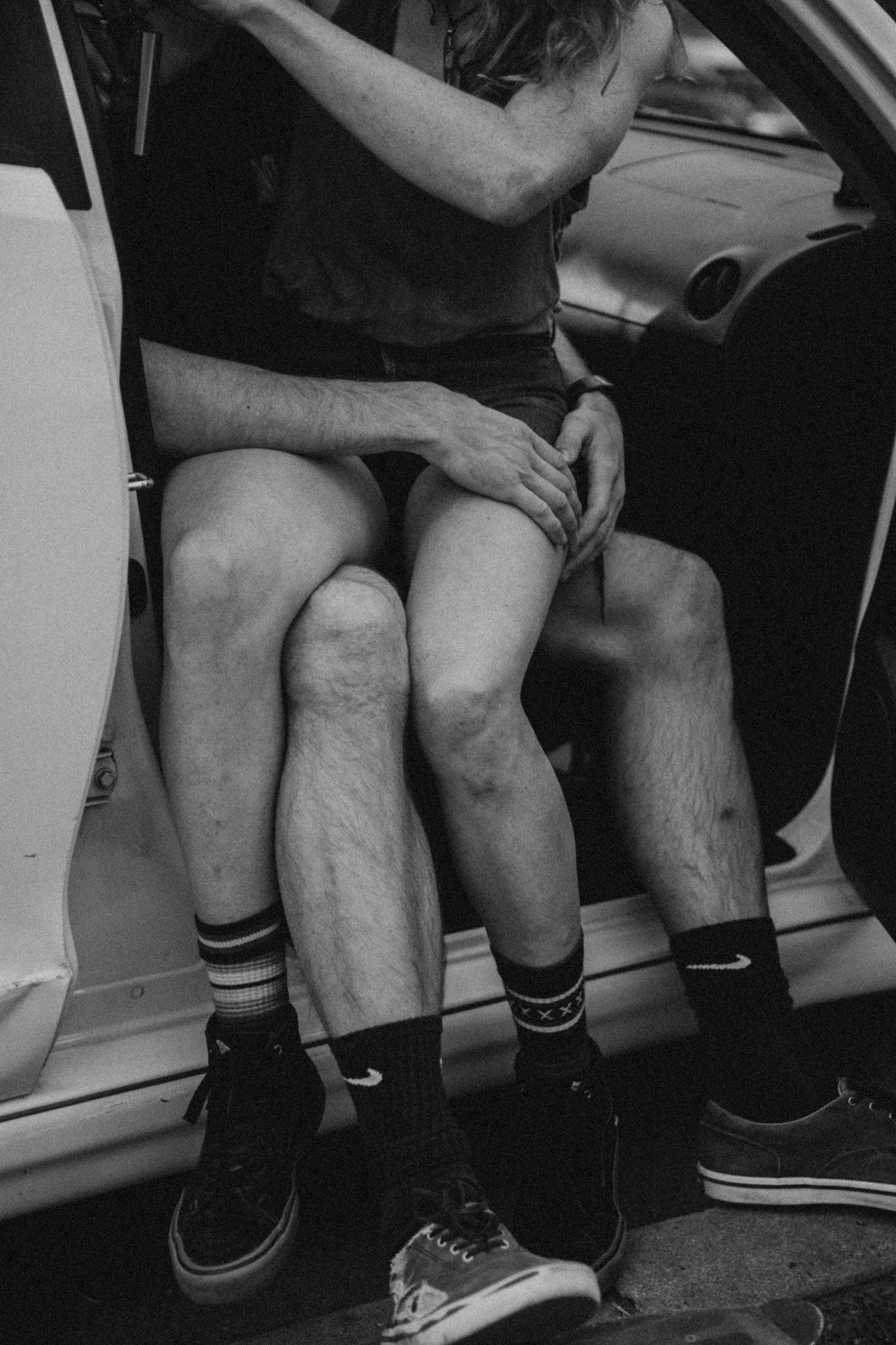 A black and white photo of people sitting in a car wearing casual clothes and socks.