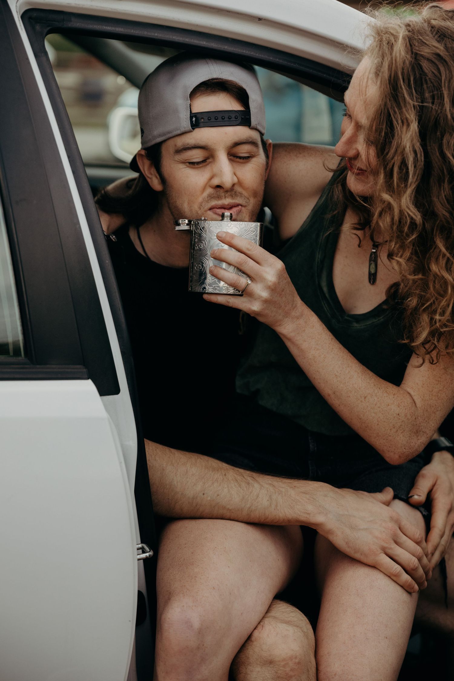 A couple sharing a drink together while sitting in a parked car.