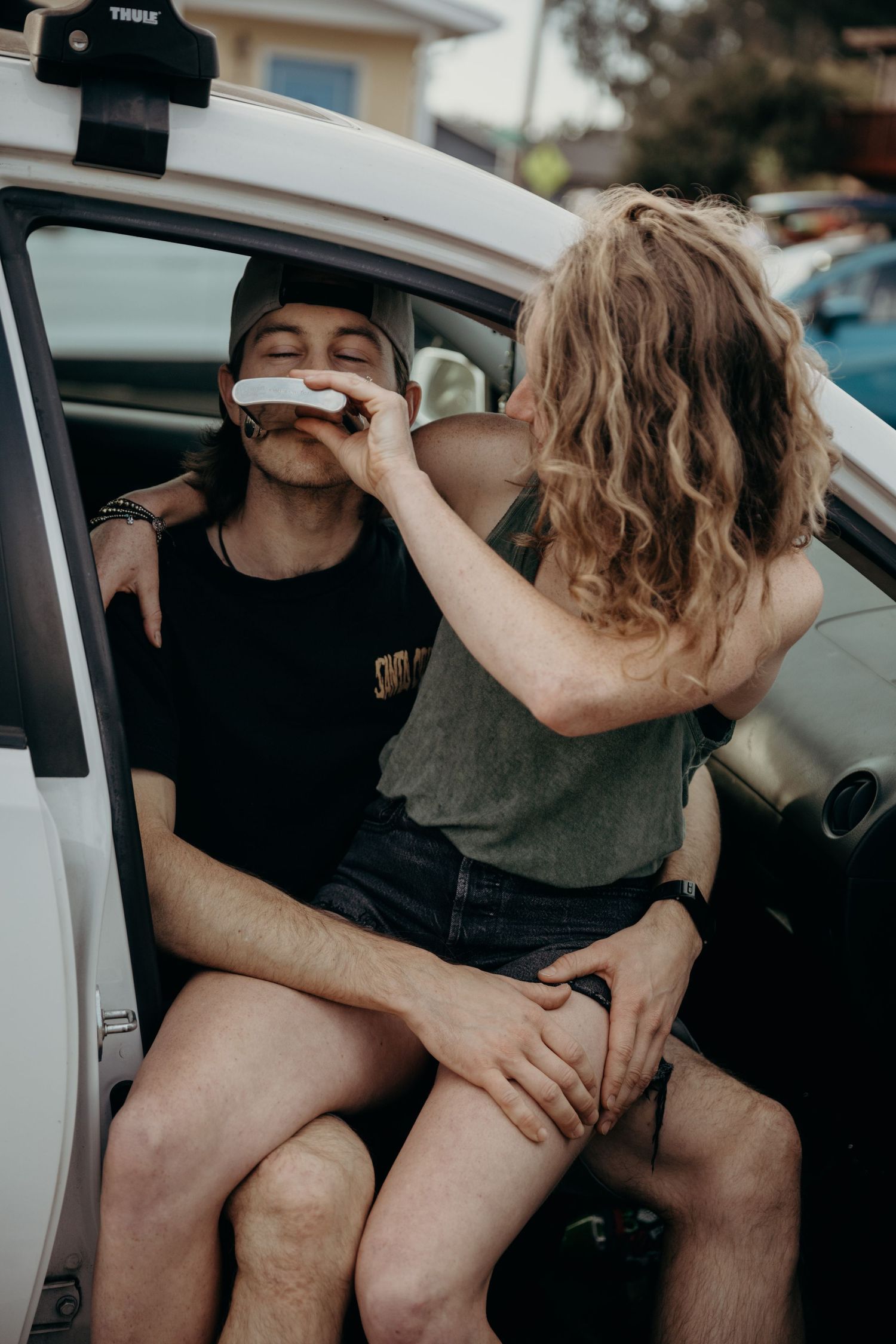 A couple sharing an intimate moment in a white car with a roof rack.