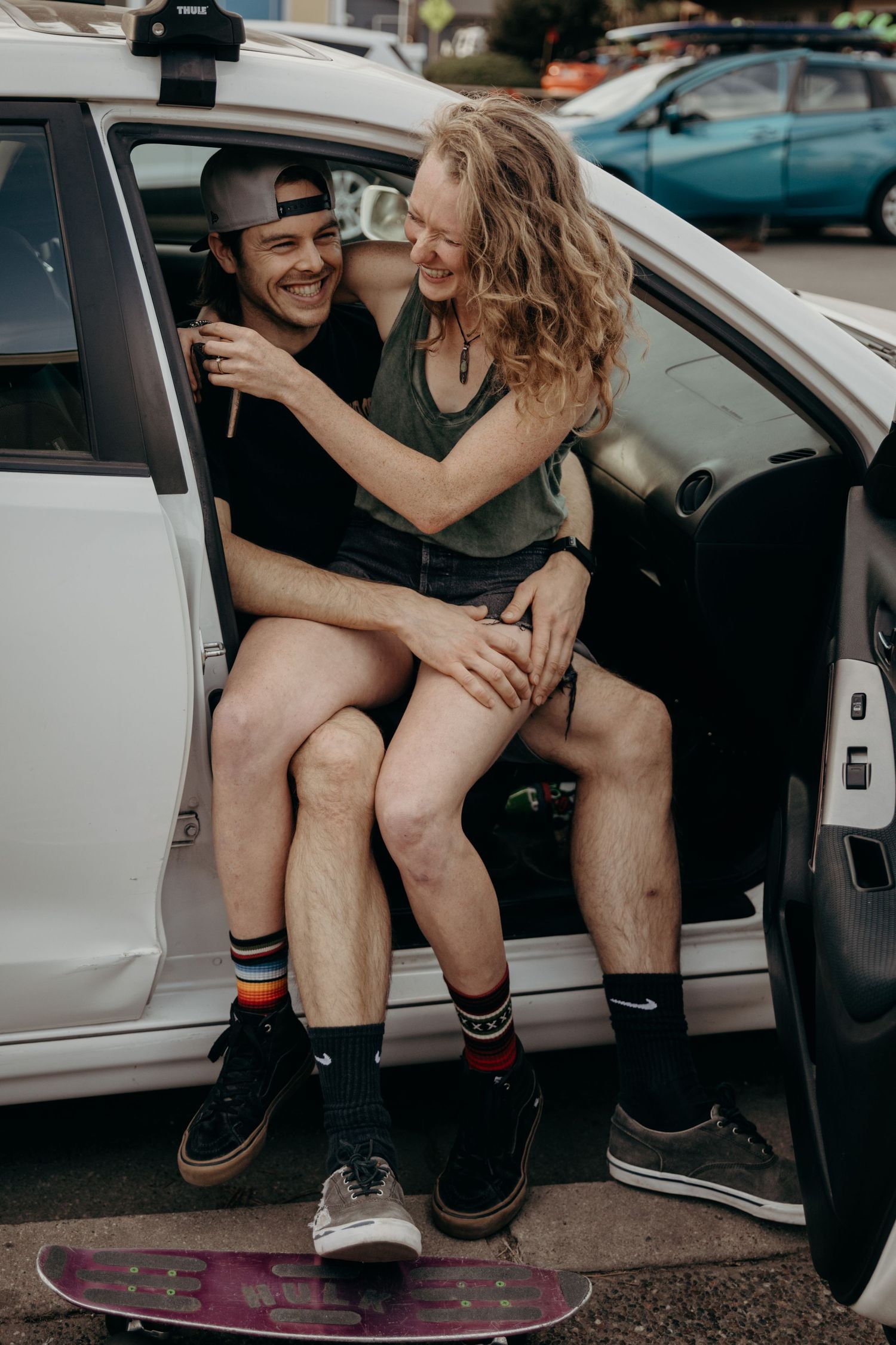 A playful moment captured between two people in a white car with a skateboard visible.