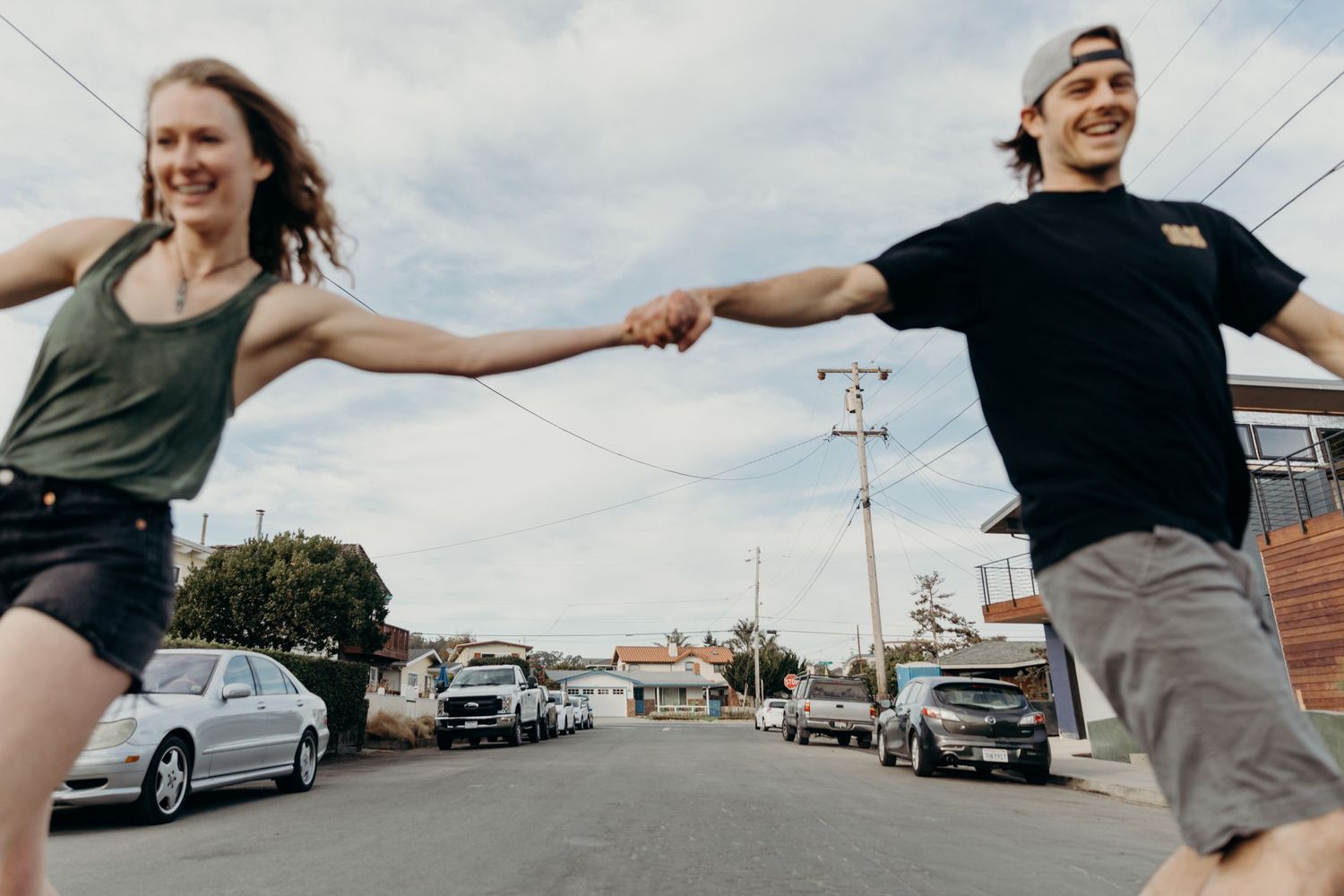 Two people holding hands while skateboarding on a city street.