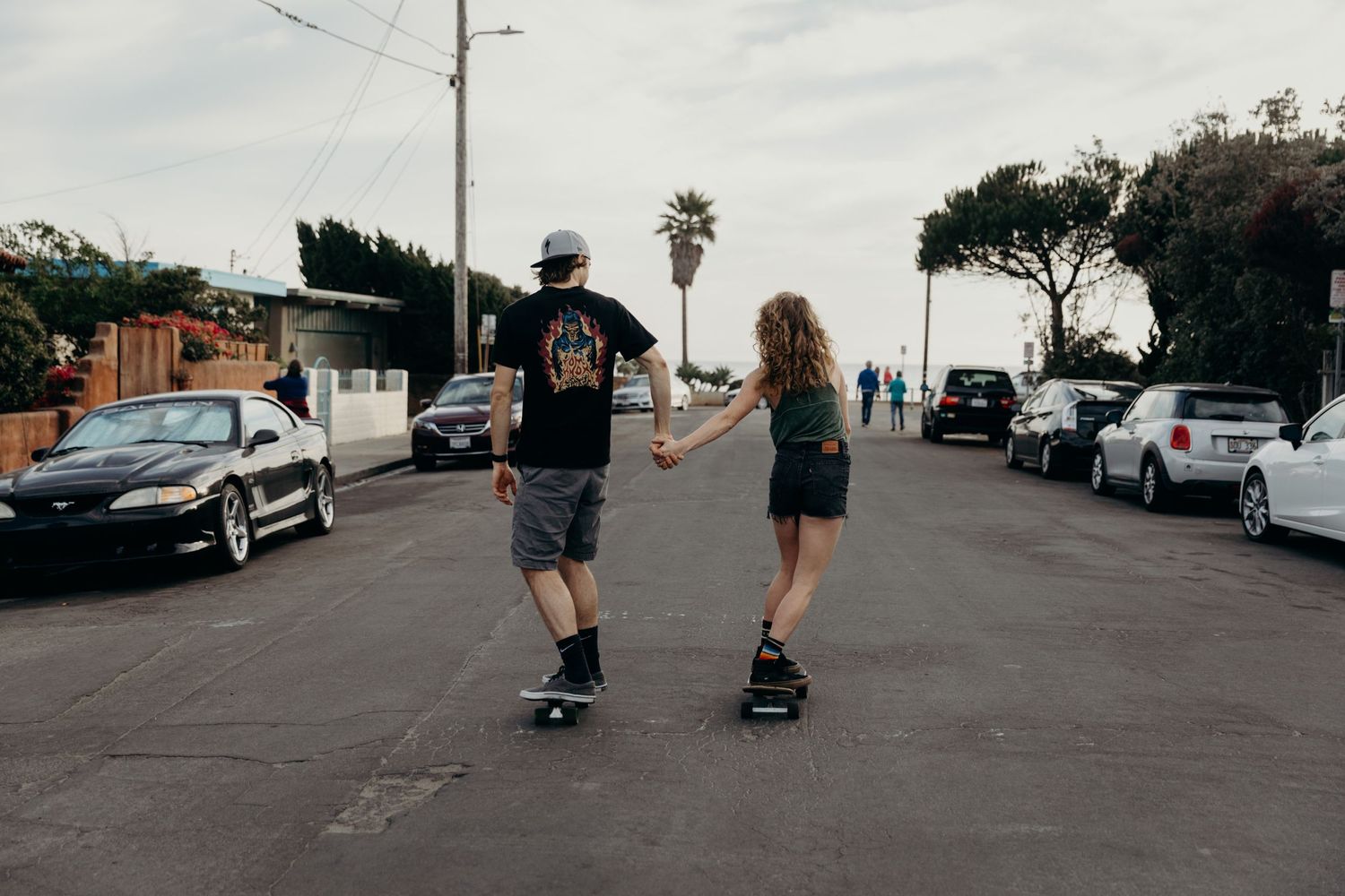 Two people skateboarding together on an urban street with parked cars.