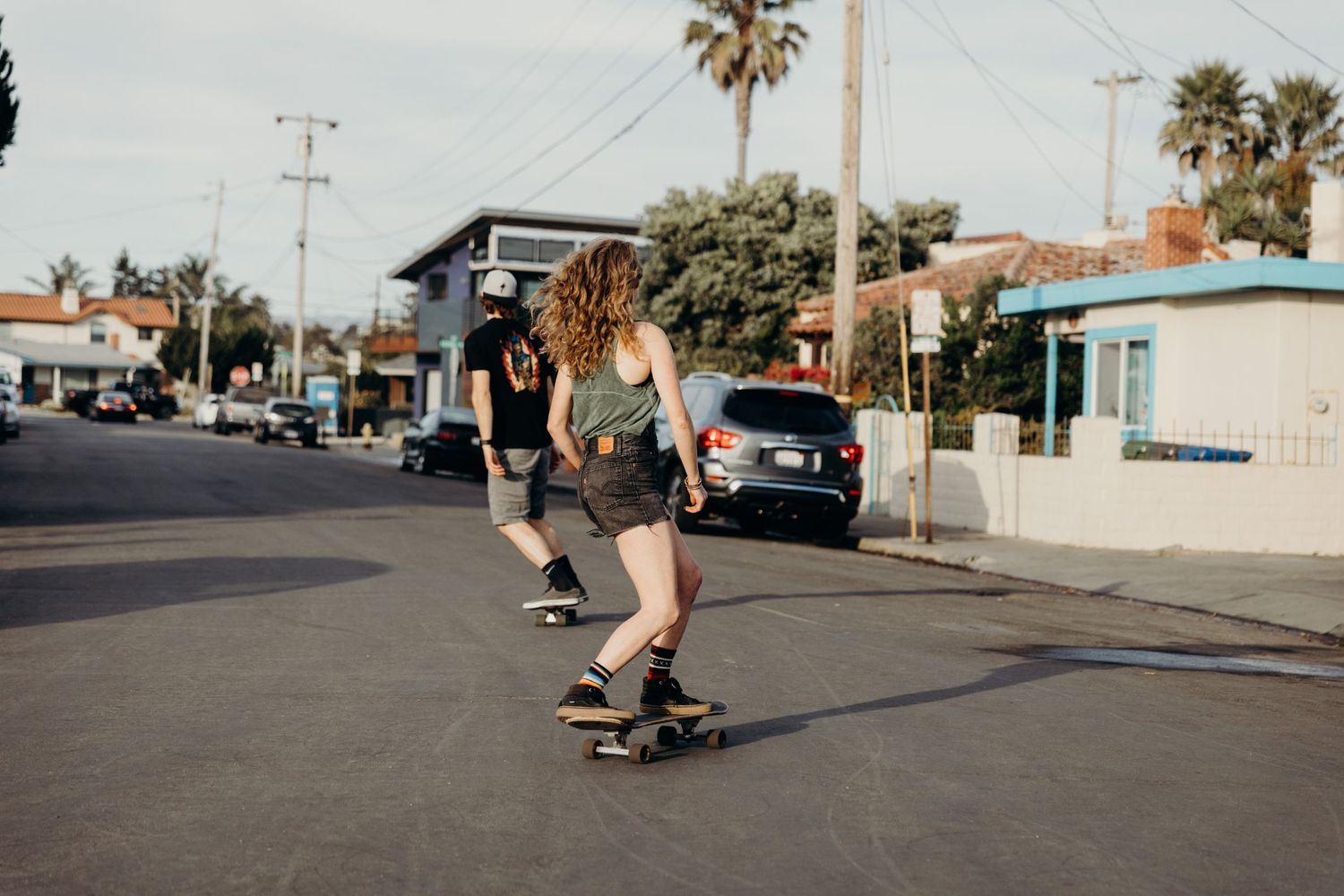 Skateboarding action shot on a sunny street with palm trees and buildings in the background.