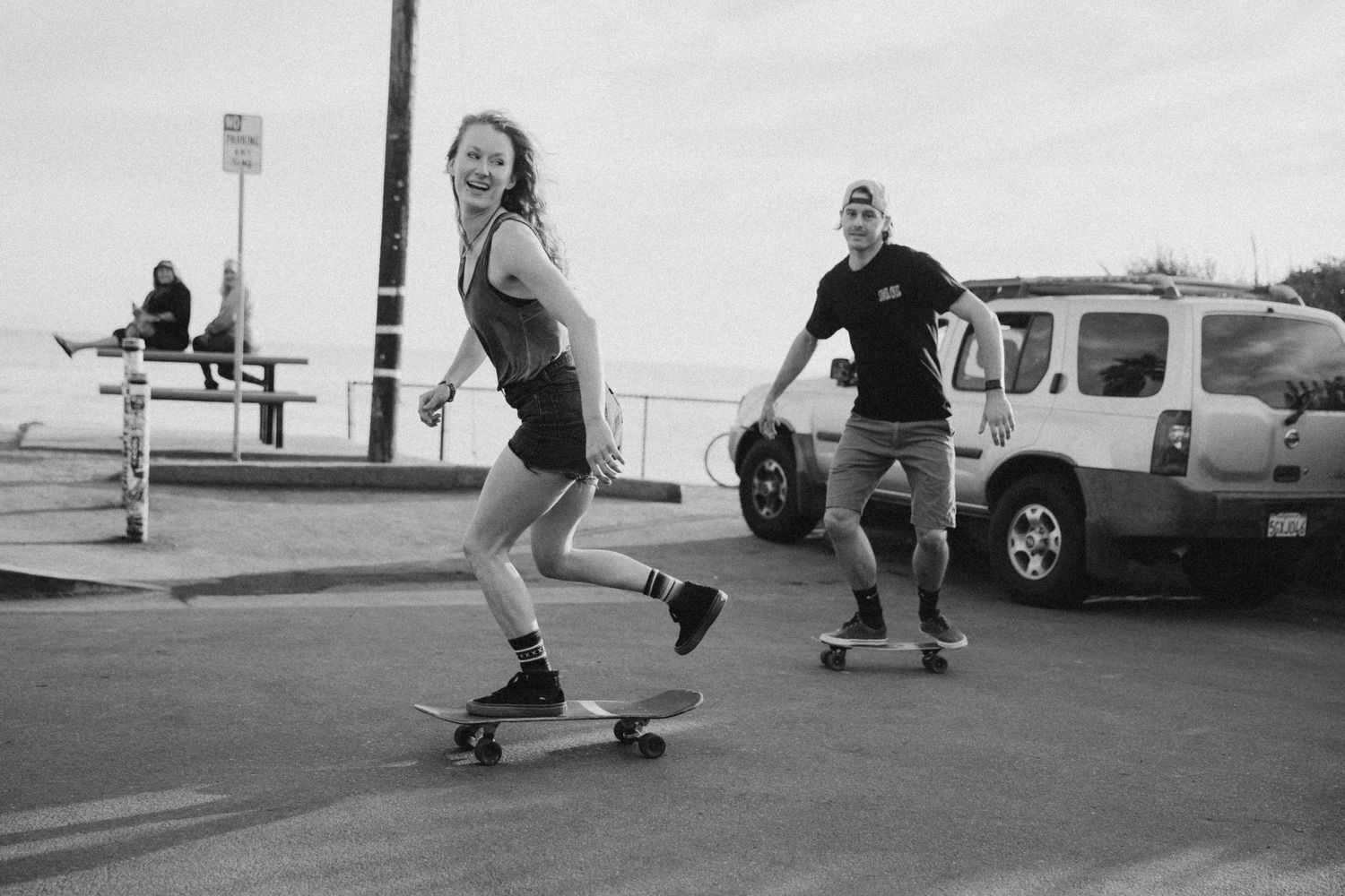 Black and white photo of skateboarding in a parking lot near the ocean.