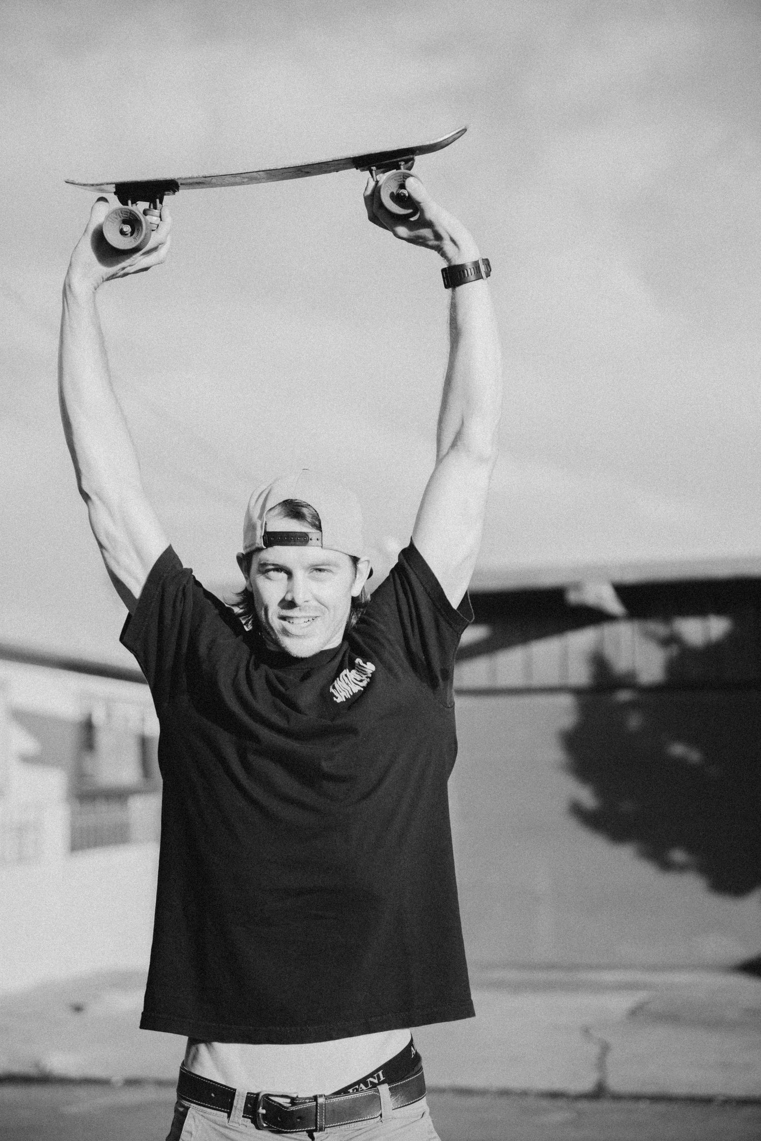 Black and white portrait of someone holding a skateboard overhead in victory pose.