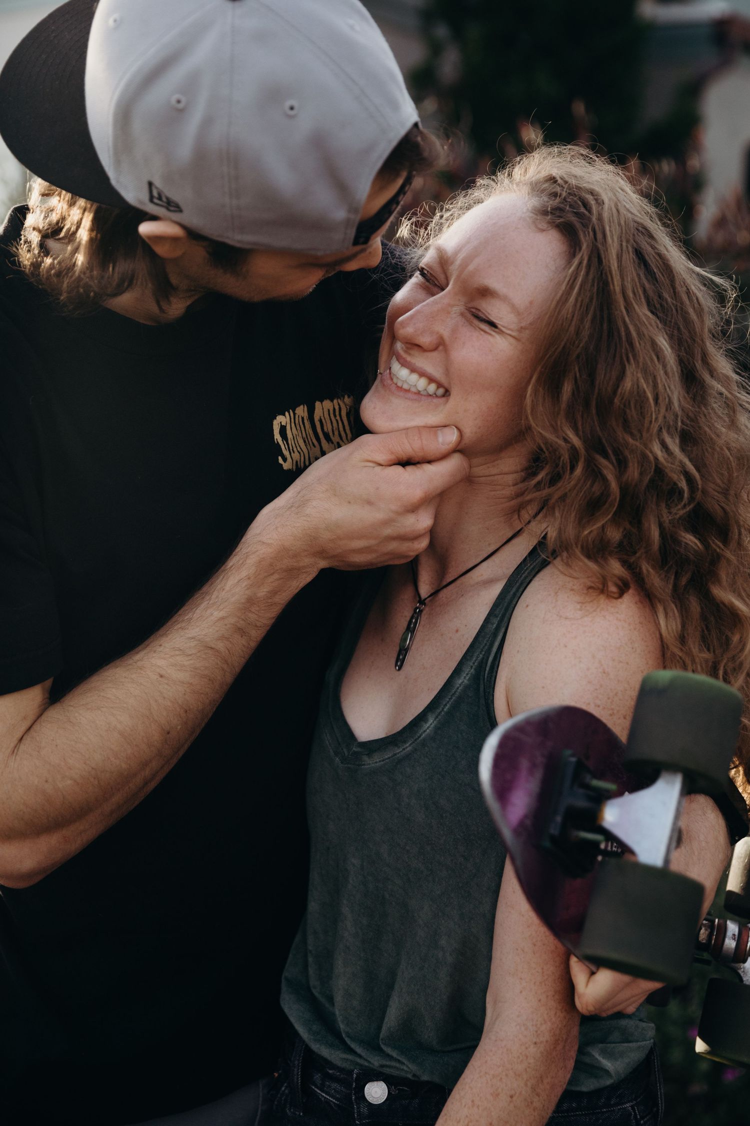 Intimate moment between couple with skateboard captured in warm sunset lighting.