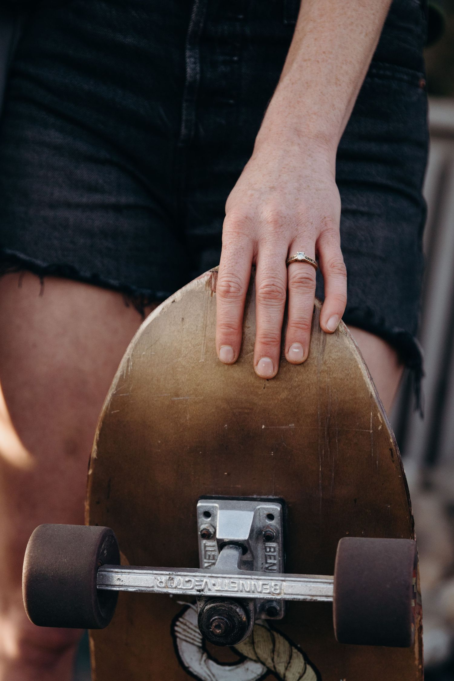 Close-up shot of hand holding wooden skateboard deck with black wheels.