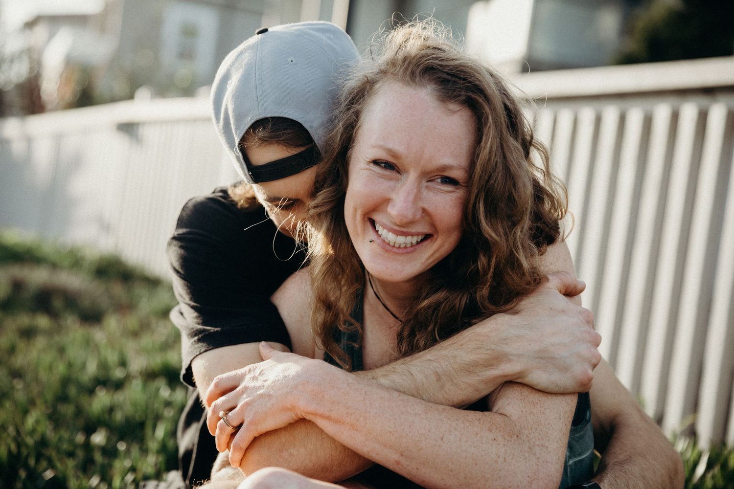 A joyful embrace captured in warm sunlight against a white fence background.