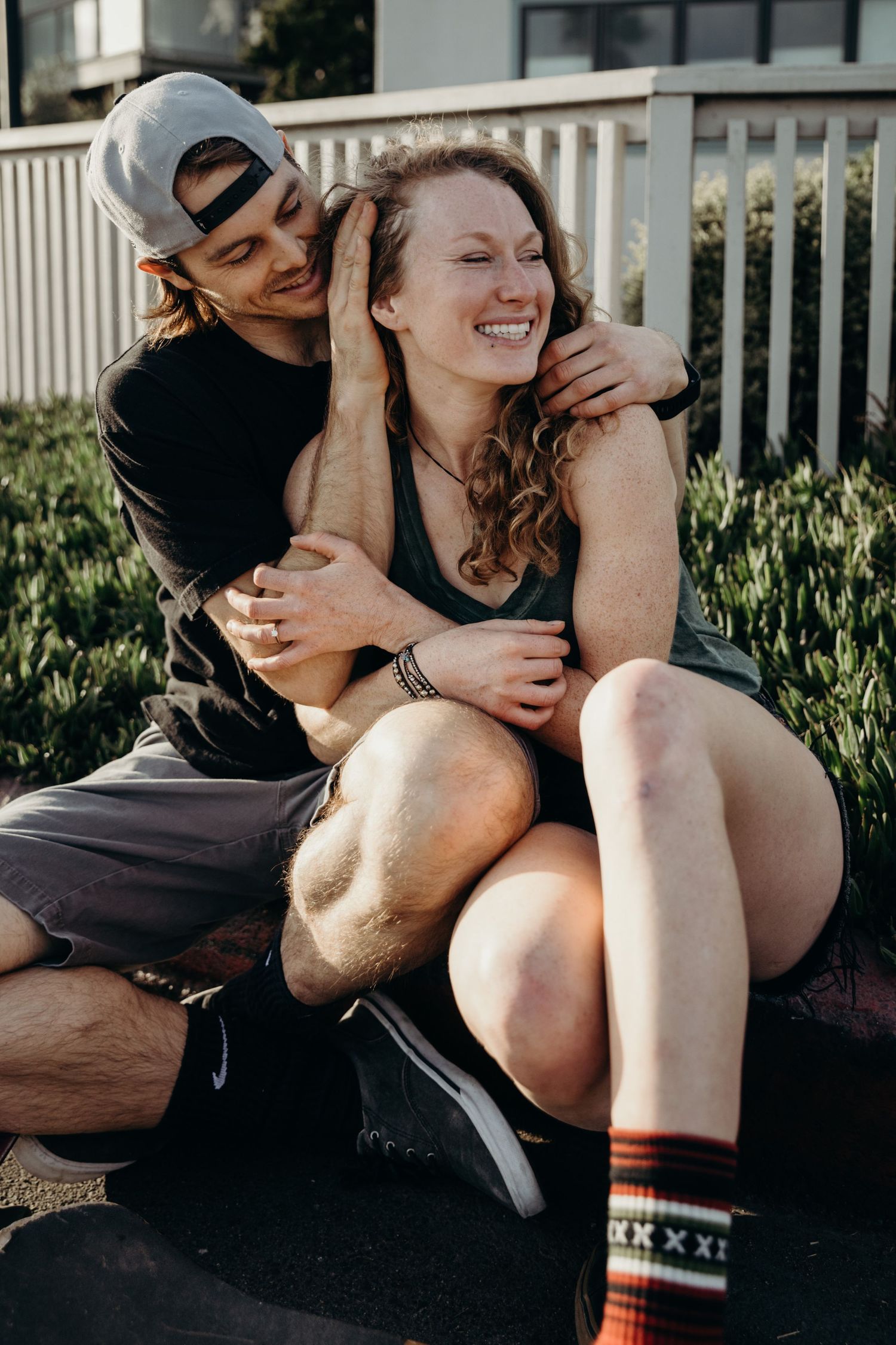 A playful couple sharing a moment while sitting on a skateboard outdoors.