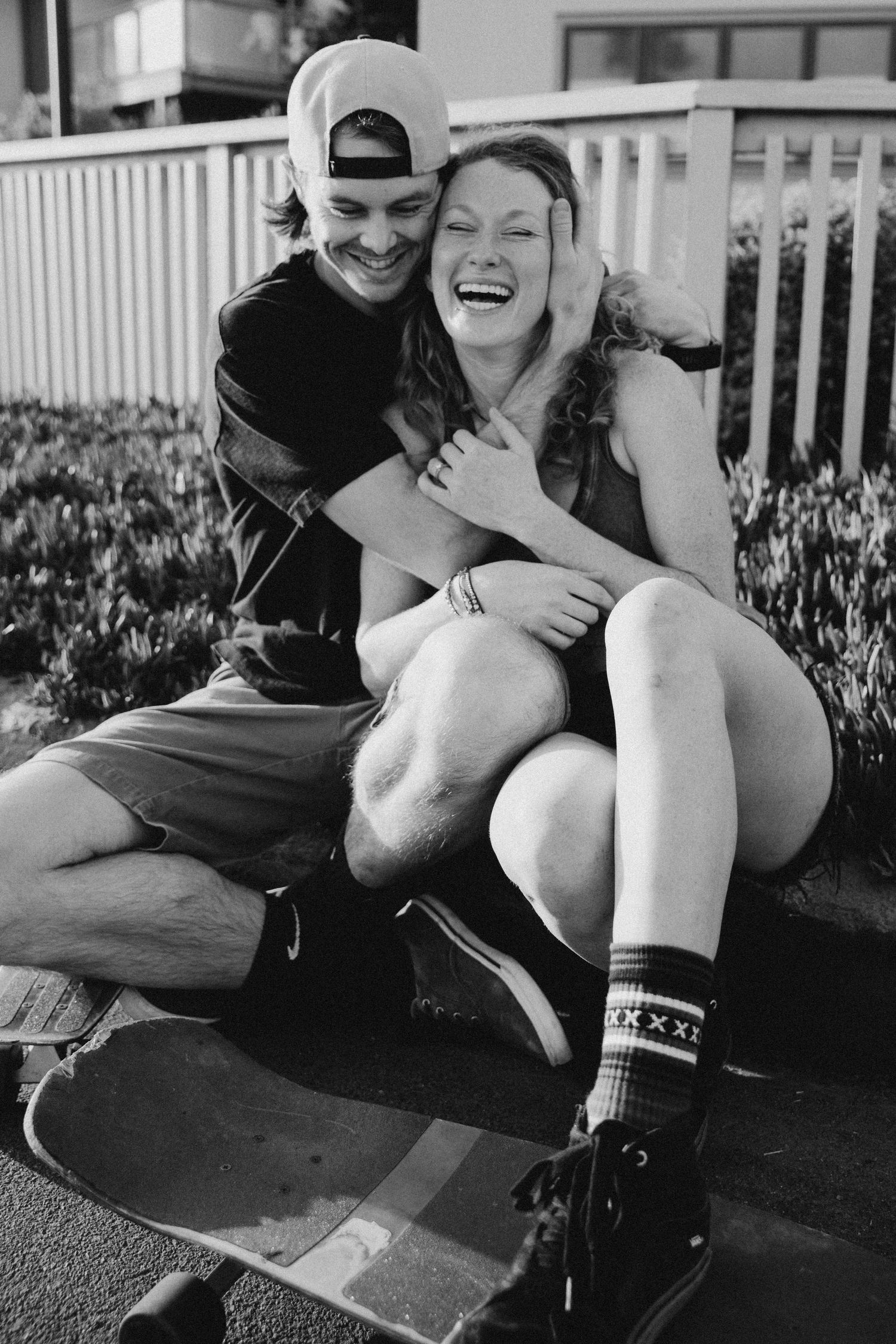 A black and white photo capturing genuine laughter and joy between a couple on a skateboard.