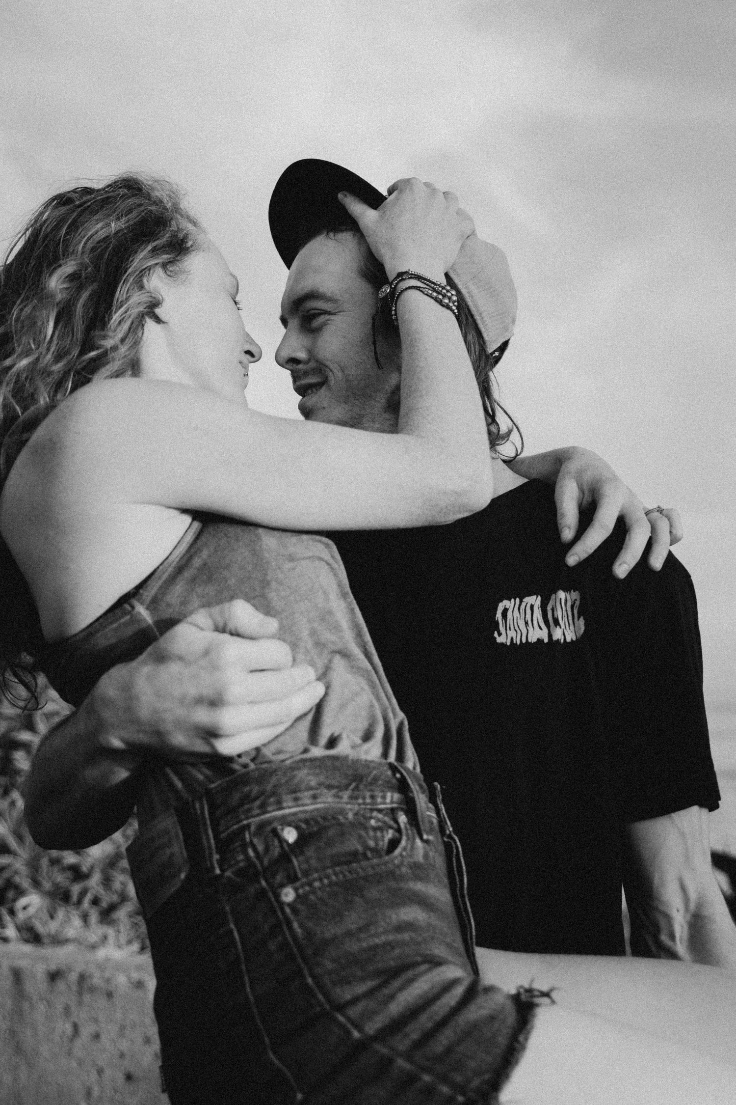 Black and white photo of couple embracing by palm trees and ocean.
