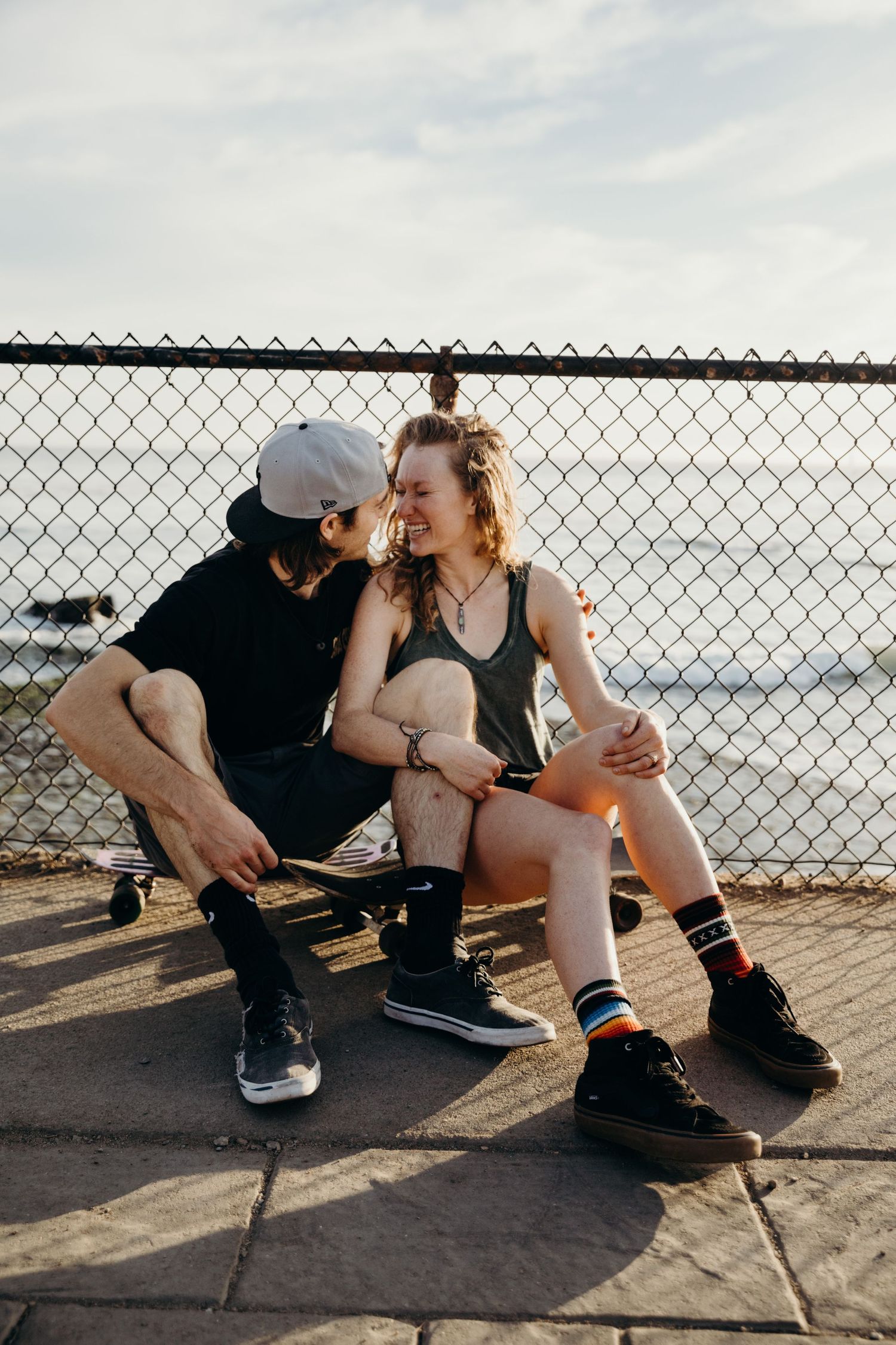 Couple sitting on fence sharing intimate moment with ocean view in background.