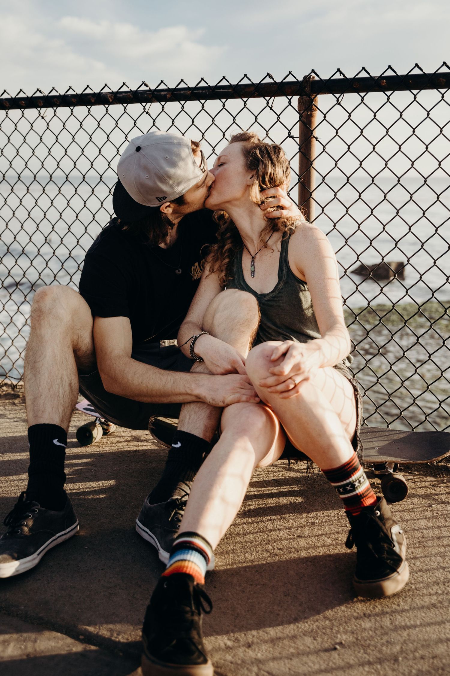 Loving couple share tender moment while sitting against chain link fence.