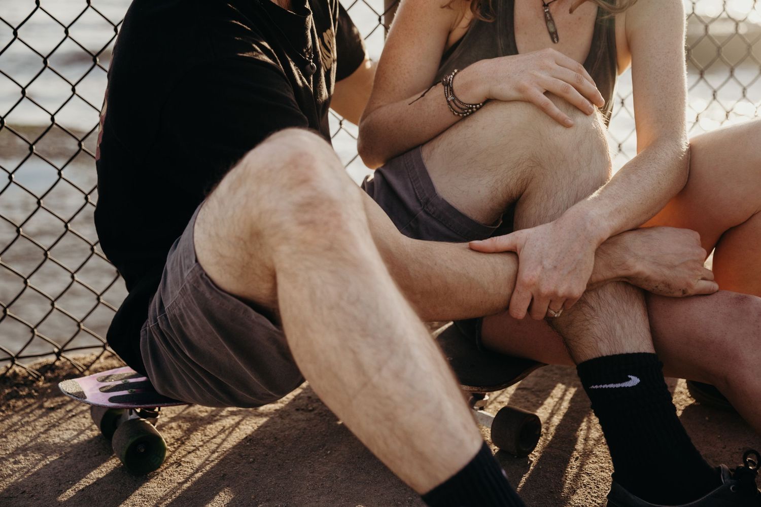 Couple sitting intimately against a chain link fence in casual athletic wear.