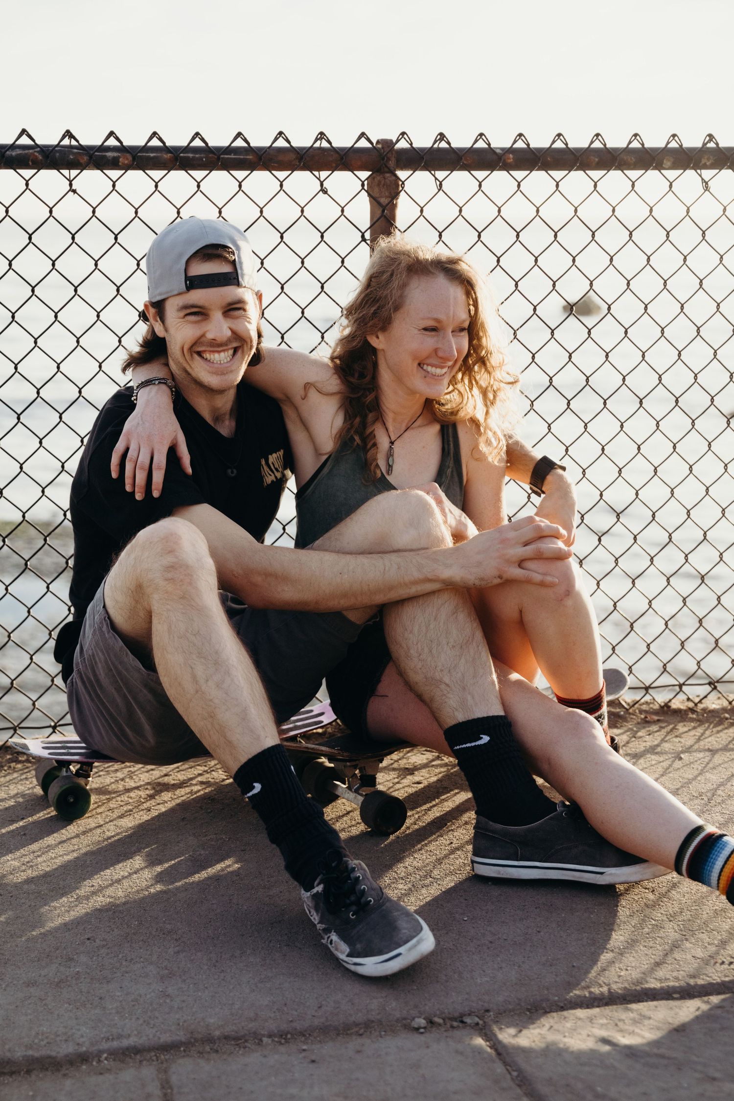 Athletic couple in workout clothes smiling together by fence.