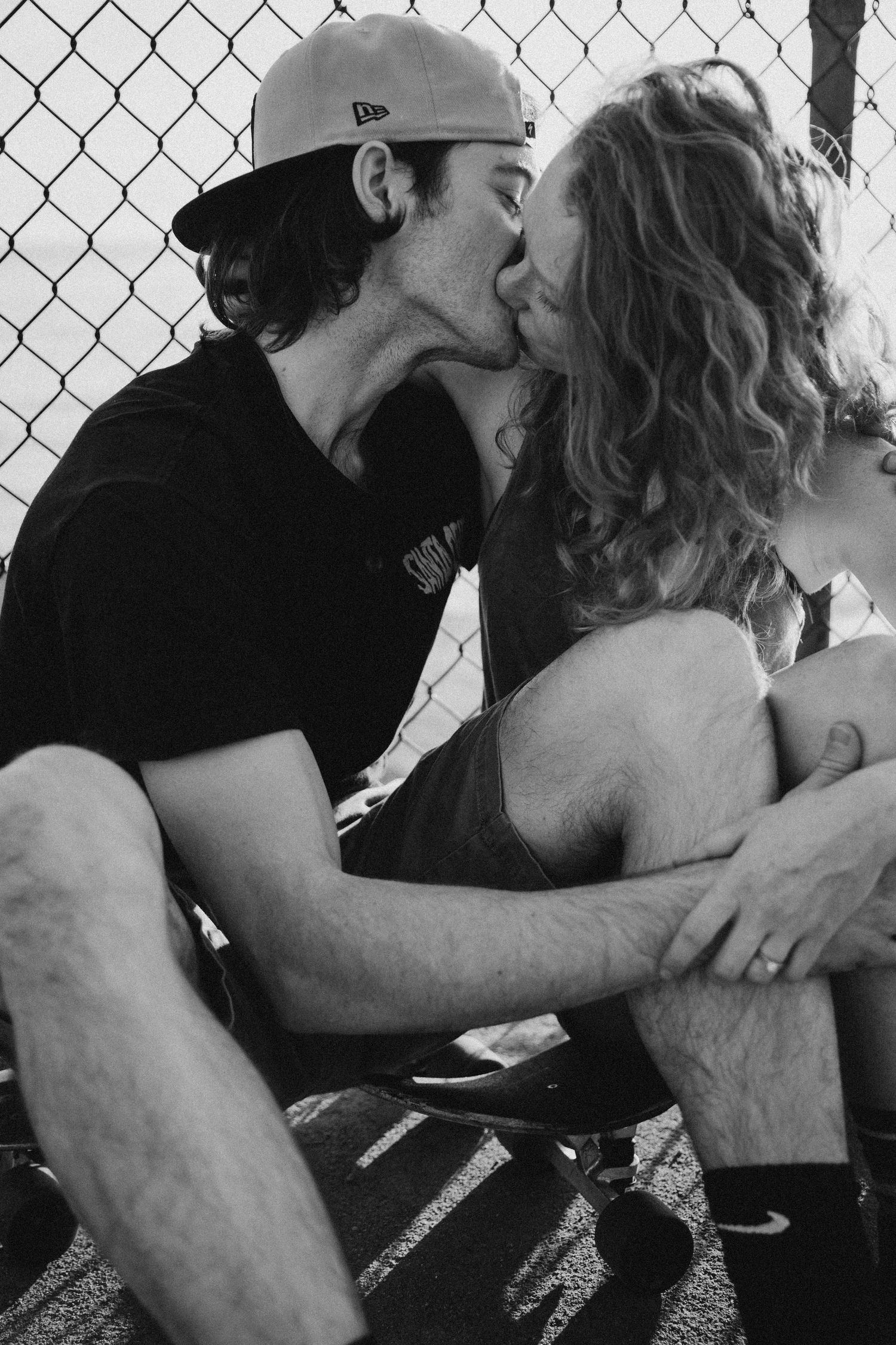 Black and white photo of romantic couple by chain link fence.